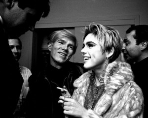 black-and-white photograph of Andy Warhol and Edie Sedgwick laughing and talking to people.